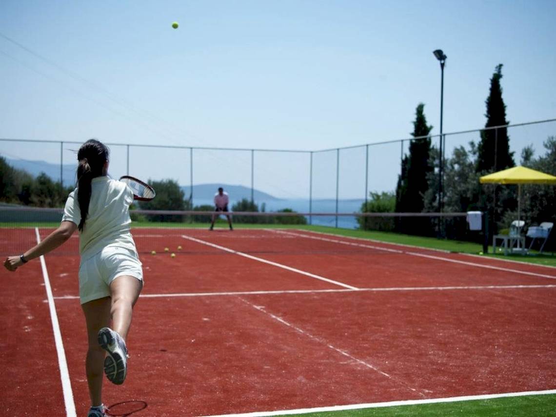 Tennisplatz im Proteas Blu Resort mit einer Frau, die den Ball schlägt.