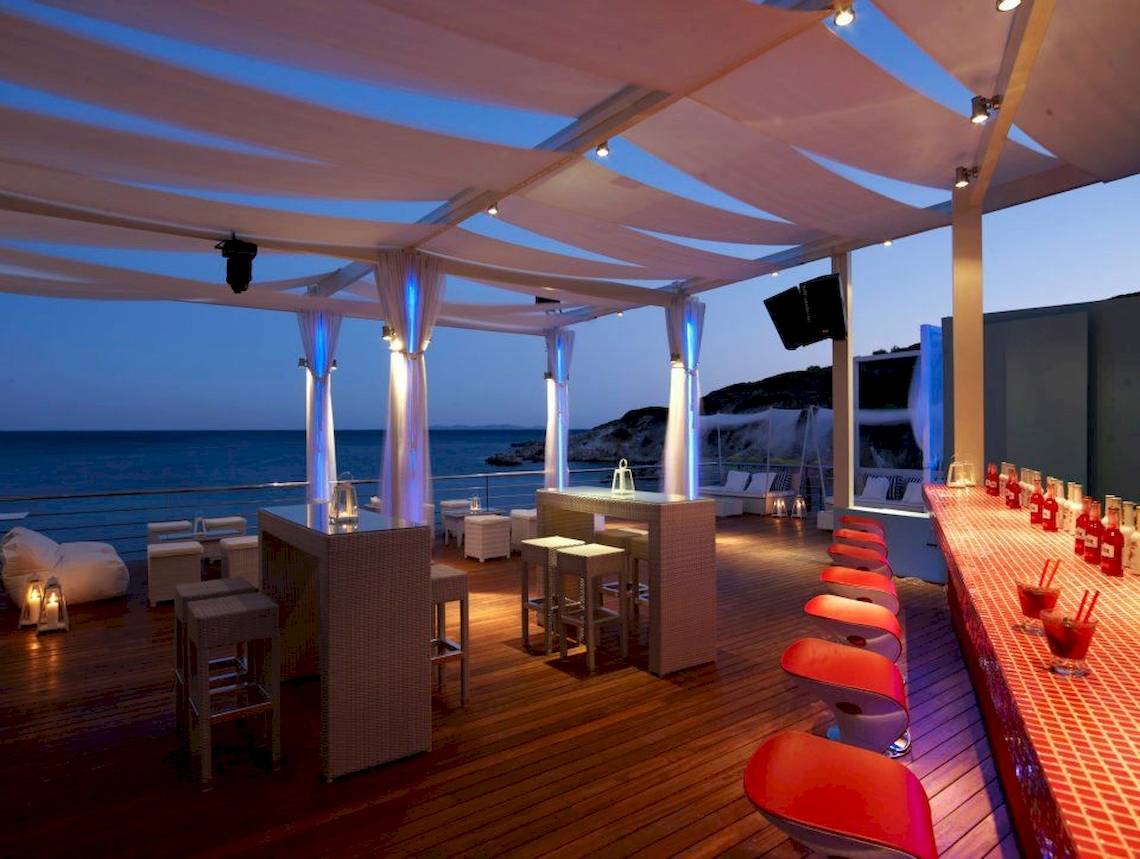 Terrasse des Proteas Blu Resorts bei Nacht mit Blick auf das Meer und roten Stühlen.