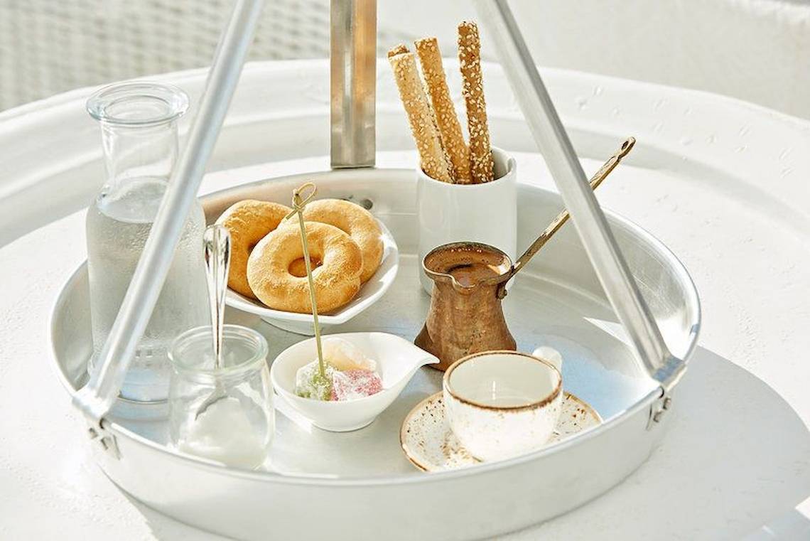 Frühstücksplatte mit Gebäck, Getränken und Zubehör auf einem runden Tablett.