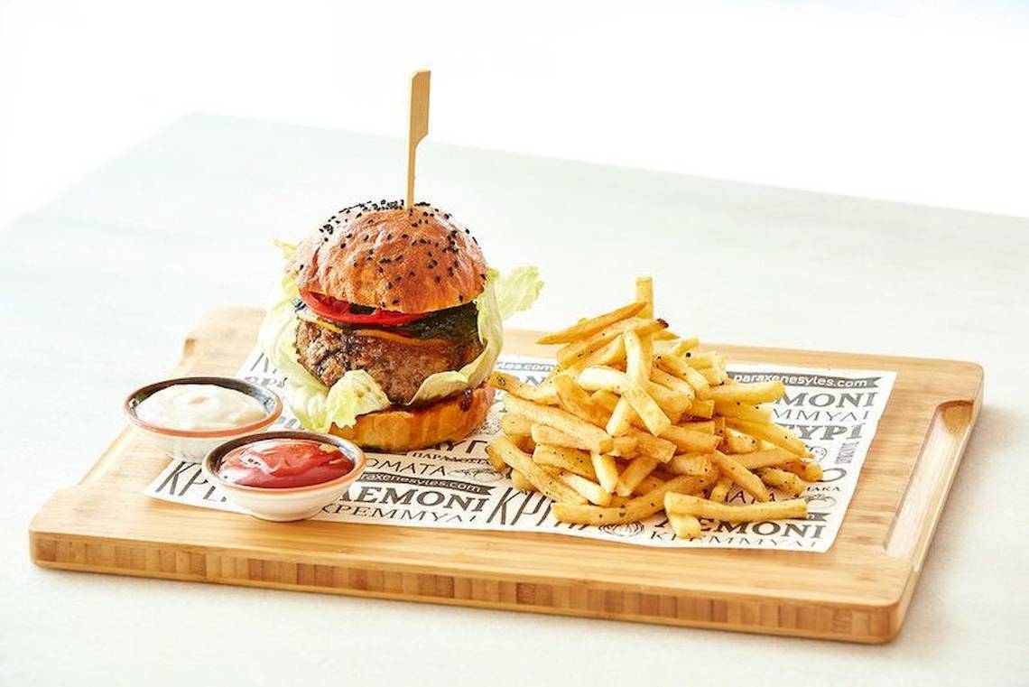 Ein Burger mit Pommes auf einem Holzbrett serviert, begleitet von Ketchup und Mayonnaise.