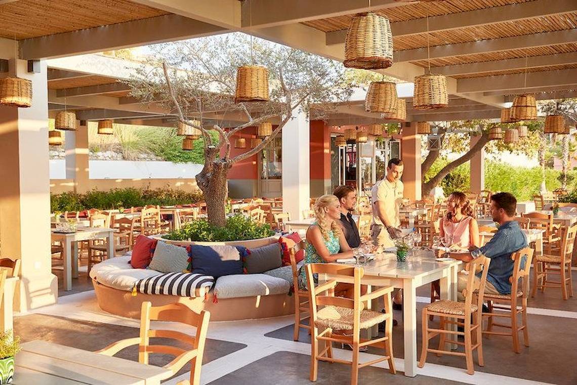Gäste sitzen an Tischen in einem freien Restaurantbereich des Grecotel Olympia Oasis Aqua Park Hotels.