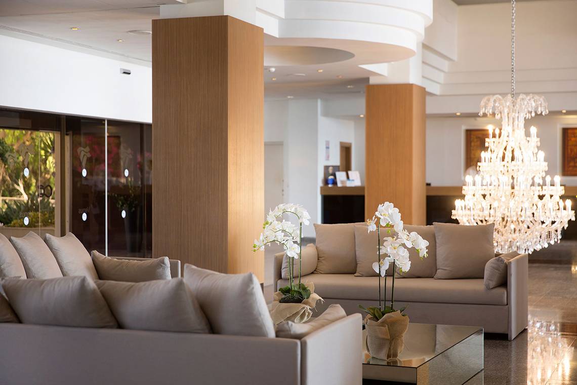 Innenansicht der Lobby im Venus Beach Hotel mit luxuriösen Sofas, weißen Orchideen und einem großen Kristall-Kronleuchter.