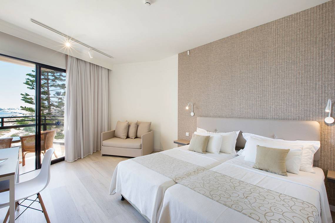 Innenansicht eines Doppelzimmers im Venus Beach Hotel mit zwei Betten, Möbeln und Balkon.