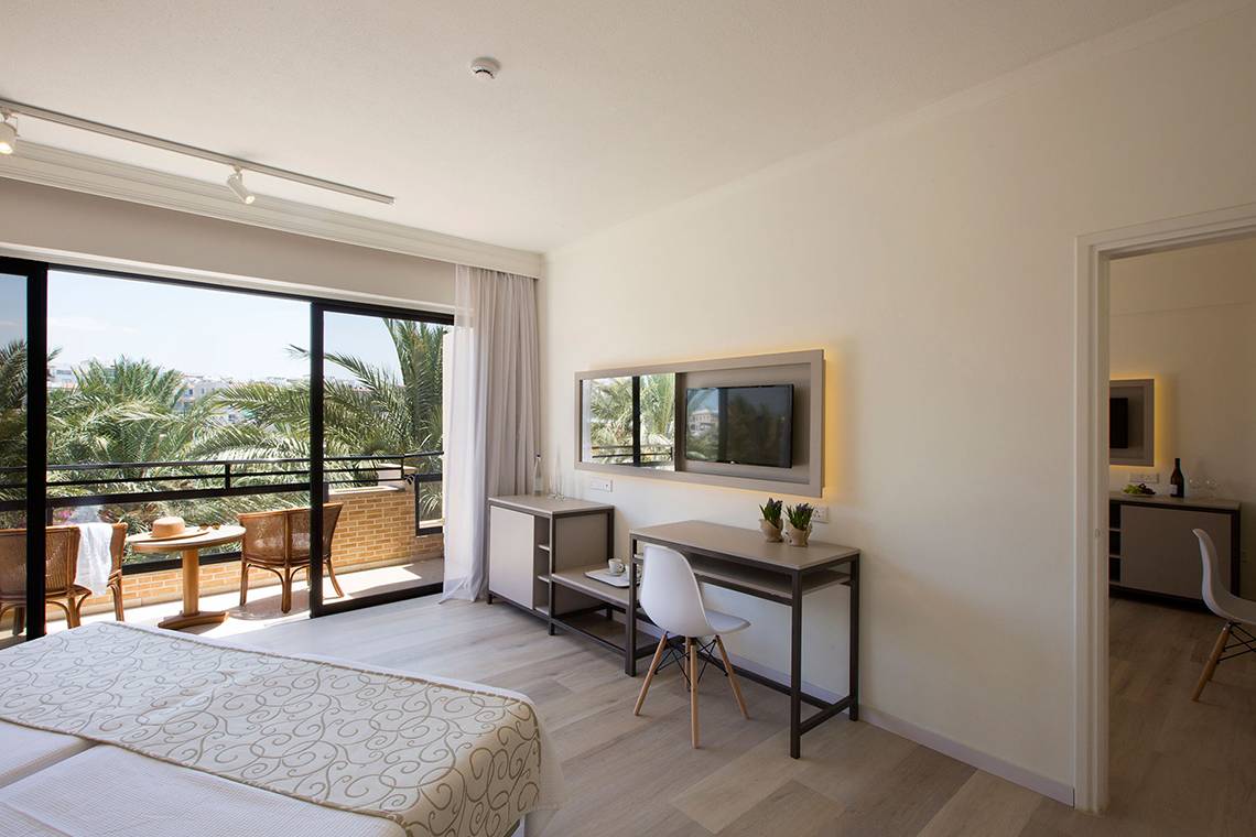 Innenansicht eines Hotelzimmers im Venus Beach Hotel mit Doppelbett, Schreibtisch und Balkon.