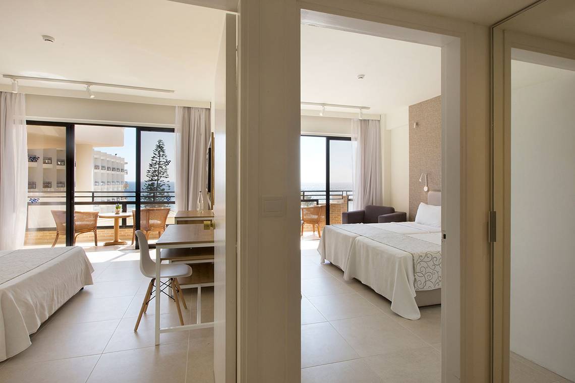 Innenansicht eines Zimmers im Venus Beach Hotel mit zwei Betten, Schreibtisch und Balkon.