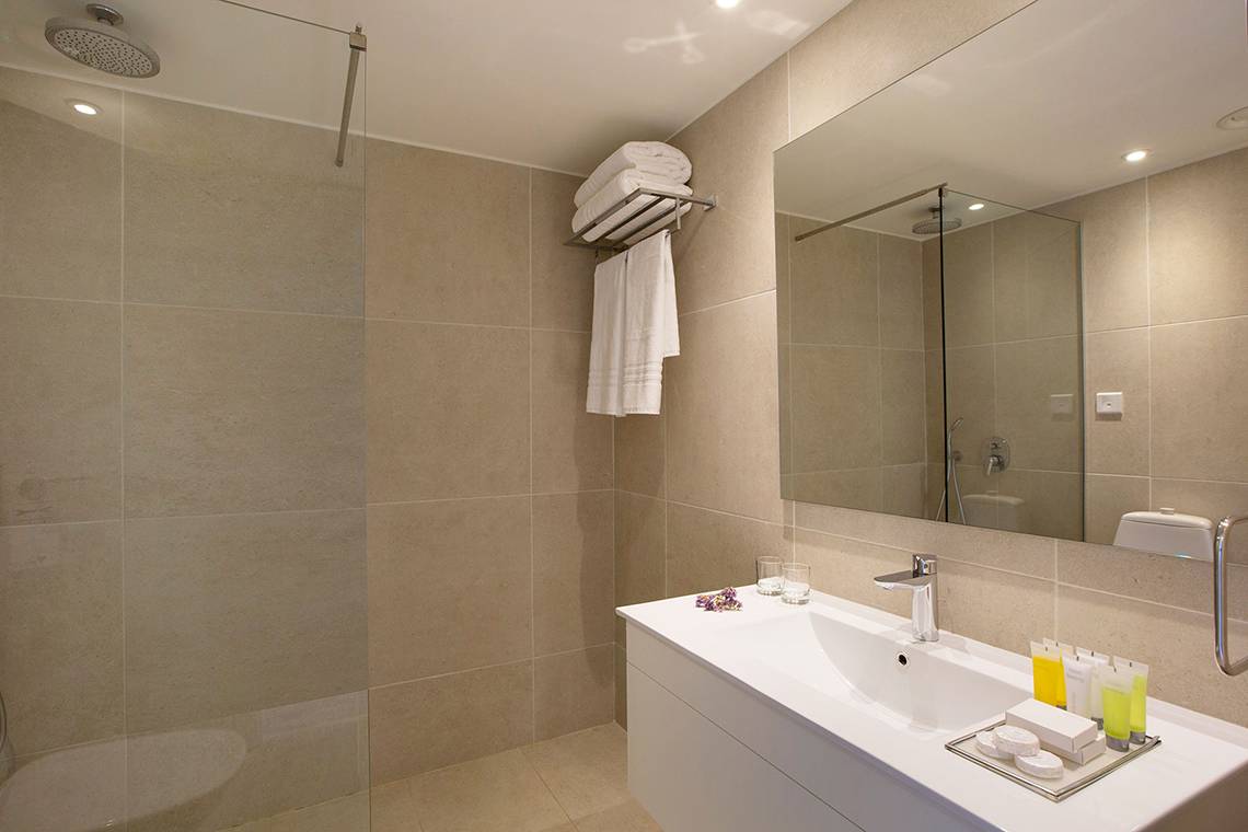 Badezimmer im Venus Beach Hotel mit Dusche, Waschbecken und Spiegel.