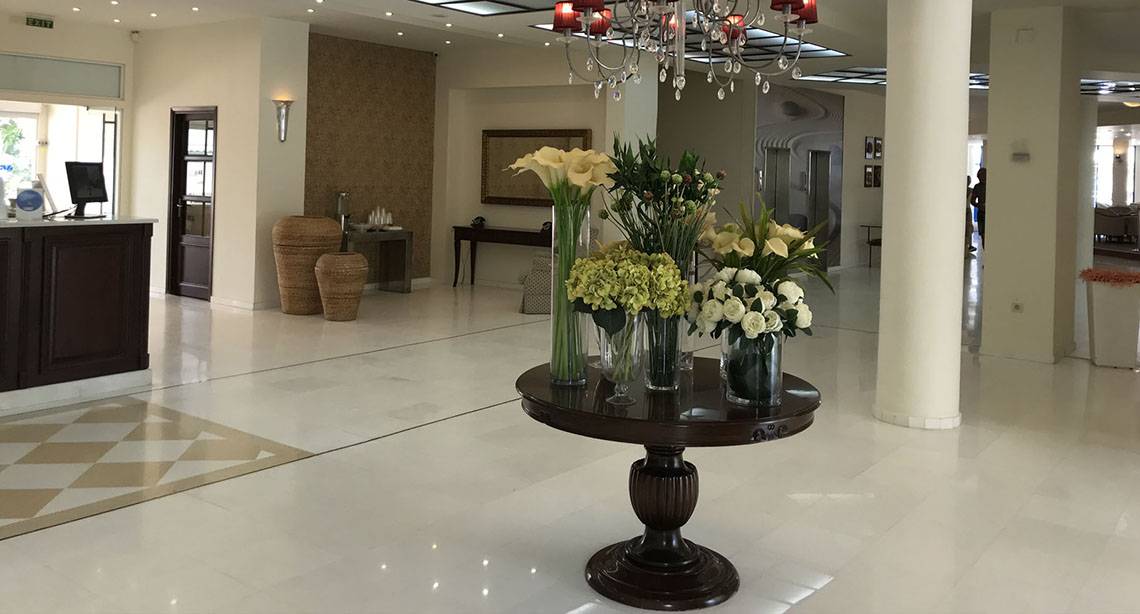Empfangsbereich des Aphrodite Beach Club Hotels mit einem zentralen Blumenarrangement auf einem runden Tisch.