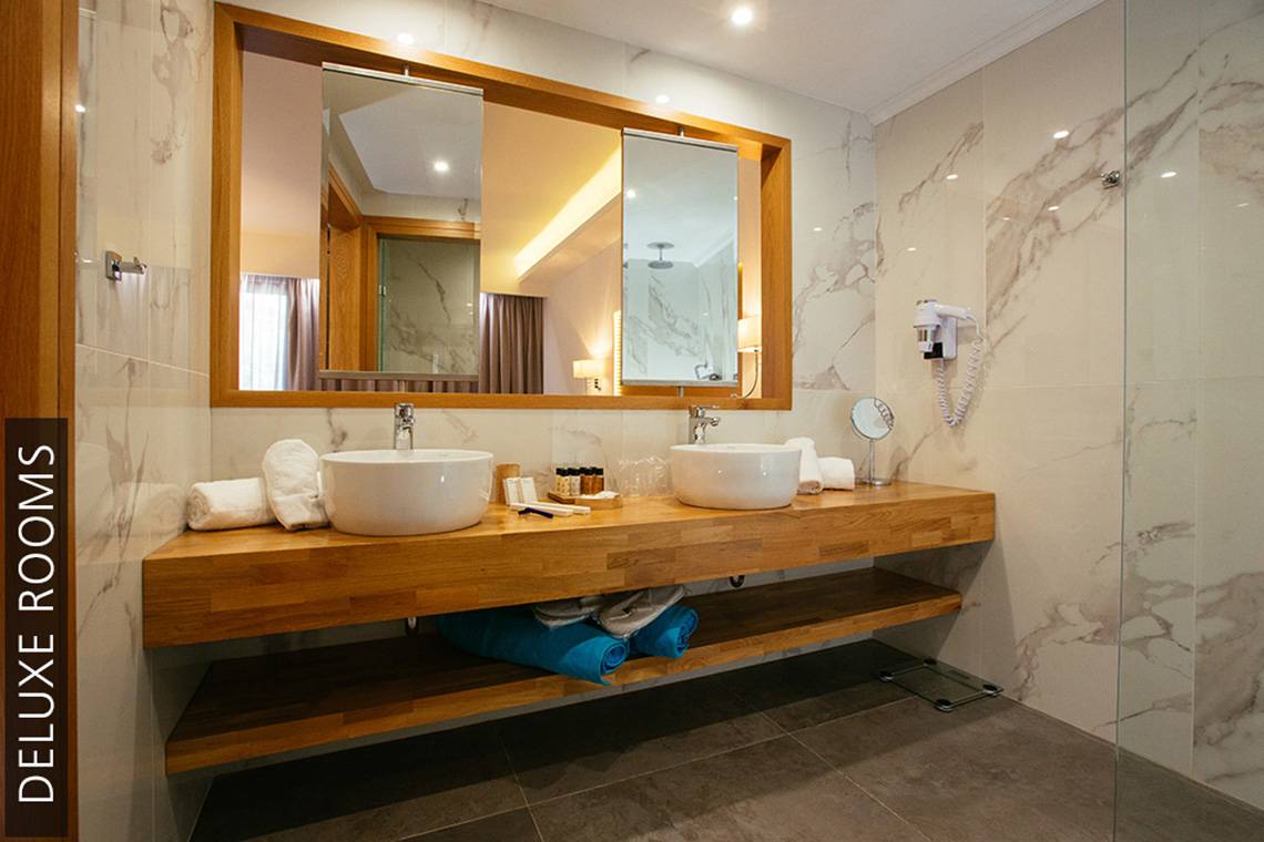 Ein Badezimmer im Aphrodite Beach Club mit zwei Waschbecken, einem Spiegel und Marmorwänden.