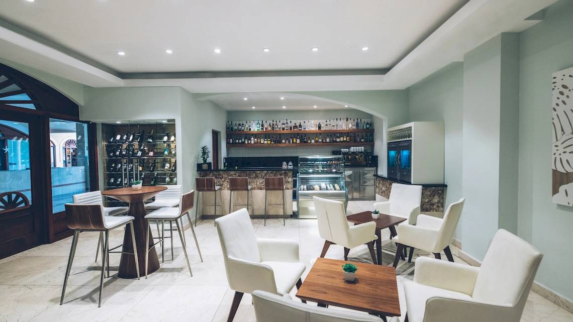 Innenbereich des Iberostar Costa Dorada Hotels mit Bar, Tischen, Stühlen und offenem Eingang.
