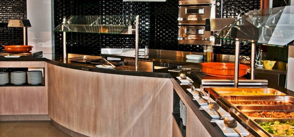 Buffetbereich im BQ Apolo Hotel mit Speisen, Geschirr und Küchengeräten.