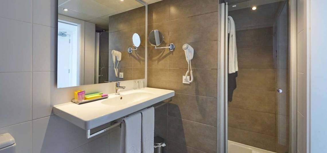 Ein Badezimmer im BQ Apolo Hotel mit einer Dusche, einem Waschbecken und einem Spiegel.
