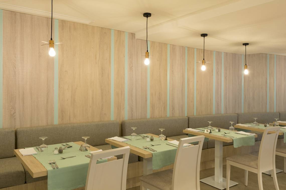 Innenraum des HSM Linda Playa Hotel Restaurants mit Holzwänden, blauen Streifen, und Tischen mit grünen Tischdecken.