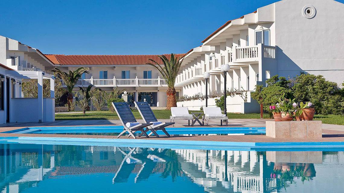 Außenpool des Mrs Chryssana Beach Hotels mit weißen Liegestühlen und Gebäuden im Hintergrund