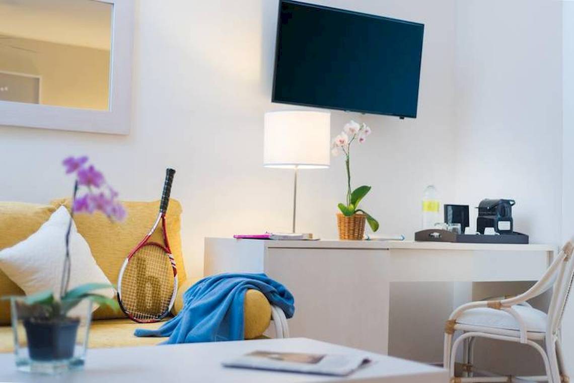 Helles Zimmer im Dreams Flora Resort & Spa mit einem Sofa, Tisch, Lampe und Fernseher.