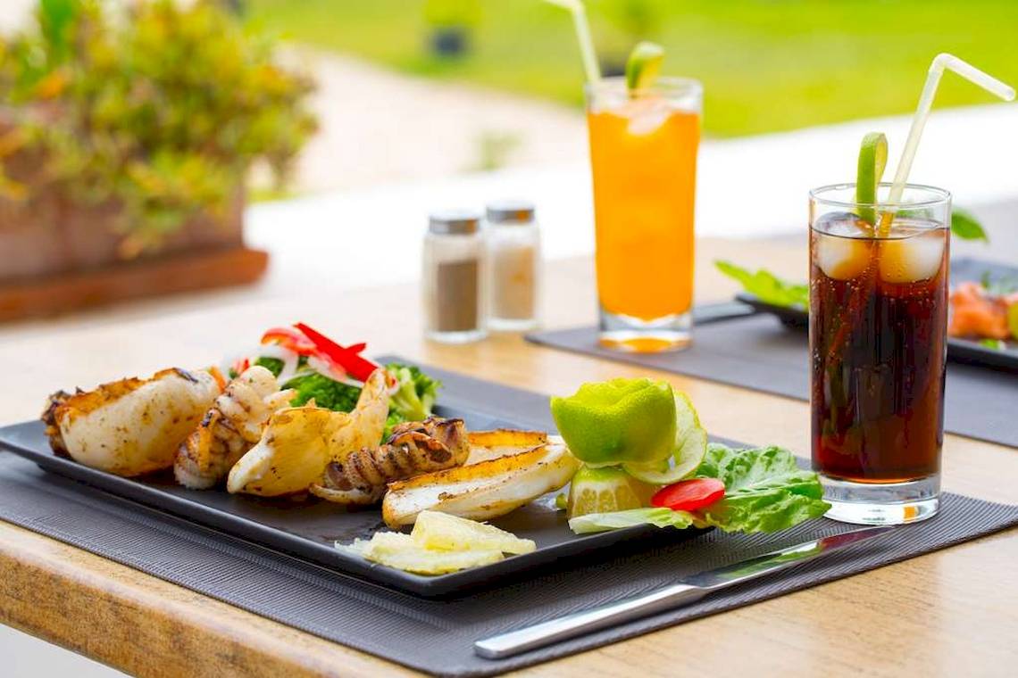 Frühstückstisch im Freien im Golden Tulip Taj Sultan mit gegrillten Meeresfrüchten, Salat, Orangensaft und Cola.