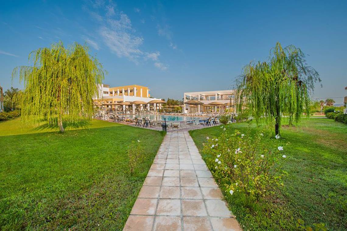 Außenbereich des Pyli Bay Hotels mit Pool, Rasen und Bäumen.