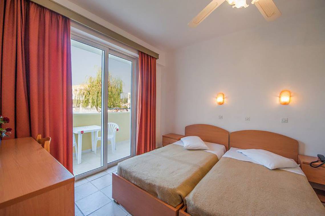 Doppelzimmer im Pyli Bay Hotel mit Balkon, zwei Betten, Schreibtisch und Fenstern.
