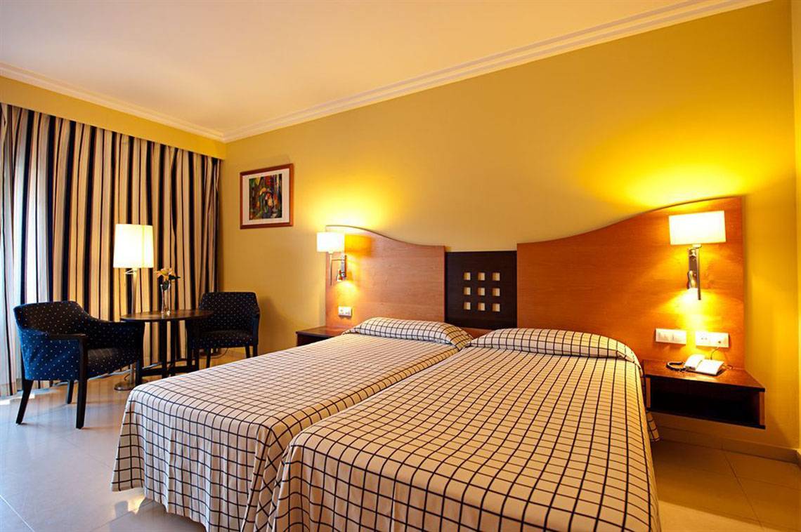 Doppelzimmer im LIVVO Costa Taurito Hotel mit zwei Betten, Stühlen und Tisch.