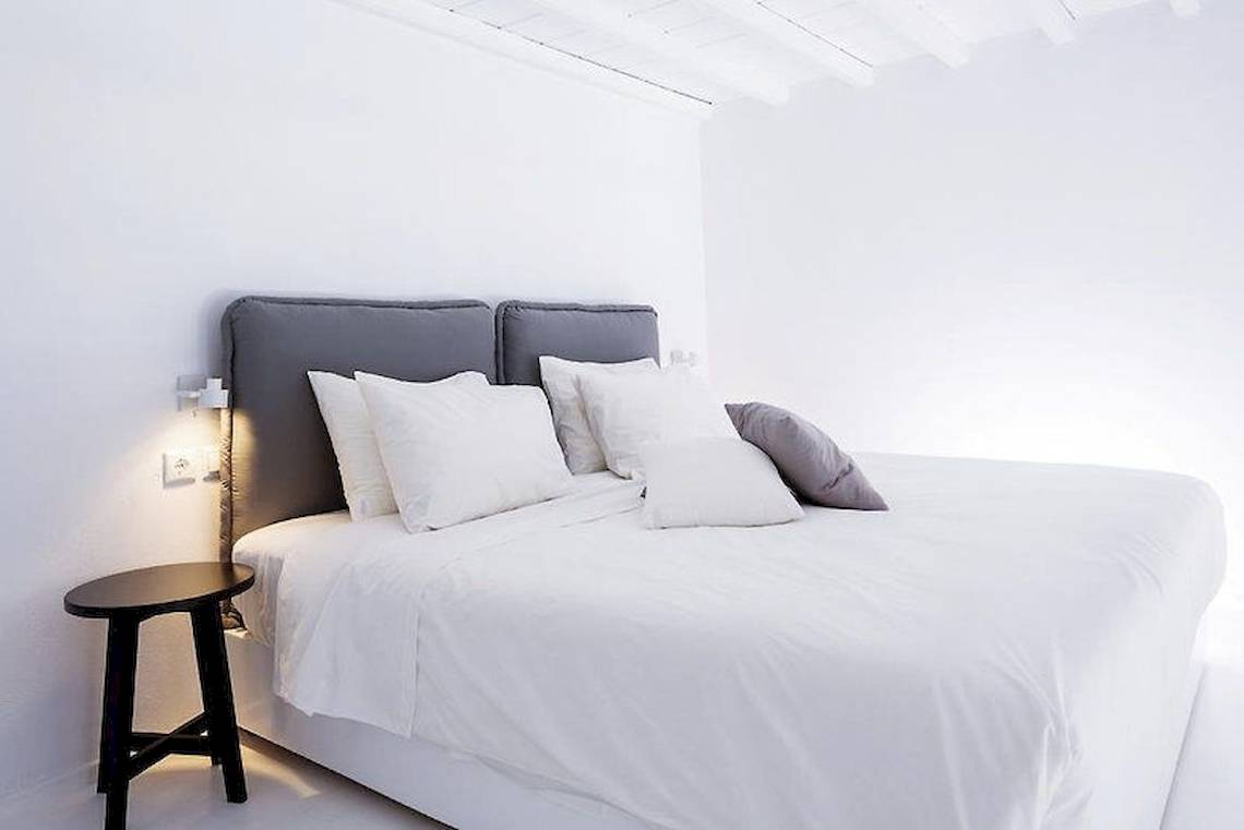 Schlafzimmer im Pietra E Mare Mykonos Hotel mit weißen Bettlaken und grauen Kopfteilen.