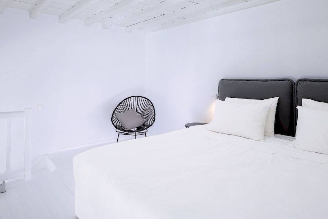Schlafzimmer im Pietra E Mare Mykonos Hotel mit weißem Bett und schwarzen Stühlen.