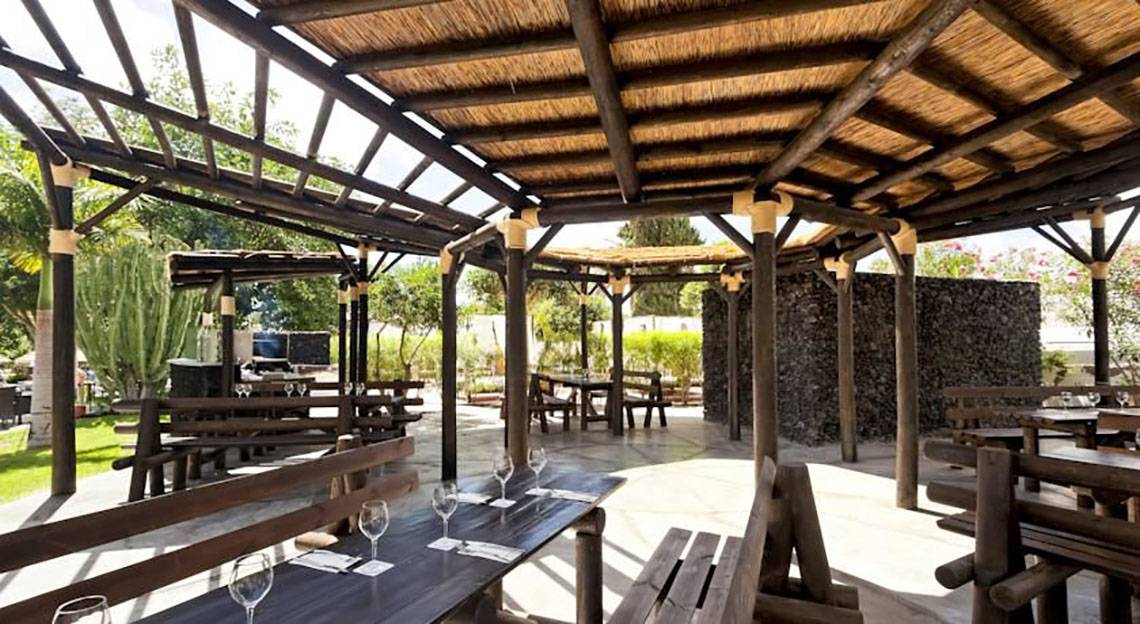 Gartenrestaurant im Barcelo Margaritas Hotel mit hölzernen Tischen und Bänken unter einem Strohdach.