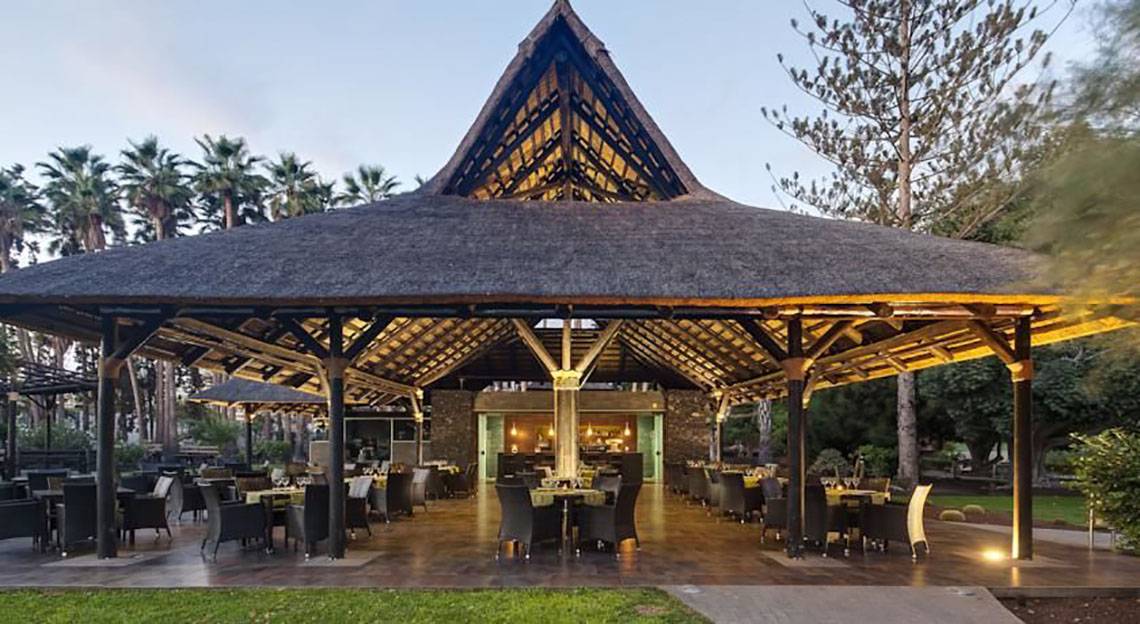 Außenbereich des Restaurants Barcelo Margaritas mit einem großen Strohdach und runden Tischen.