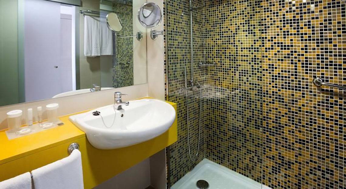Ein Badezimmer mit einer gelben Theke, einem Waschbecken, einem Spiegel und einer gefliesten Duschkabine.