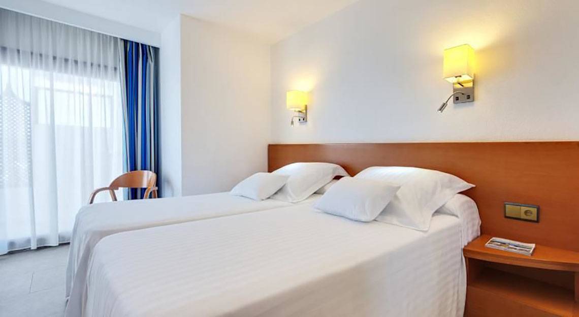 Doppelzimmer im Barcelo Margaritas Hotel mit zwei Betten, weißen Kissen, Nachttischen und Wandlampen.