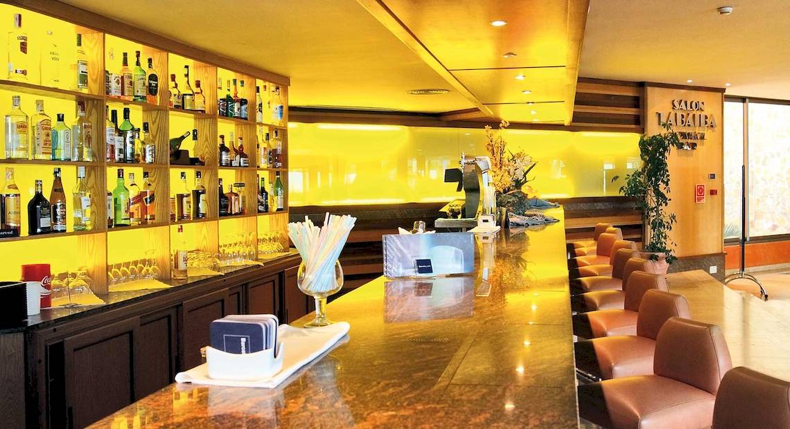 Innenansicht der Bar im Barcelo Fuerteventura Mar Hotel mit Bartheken, gefüllten Flaschen und Lederstühlen.