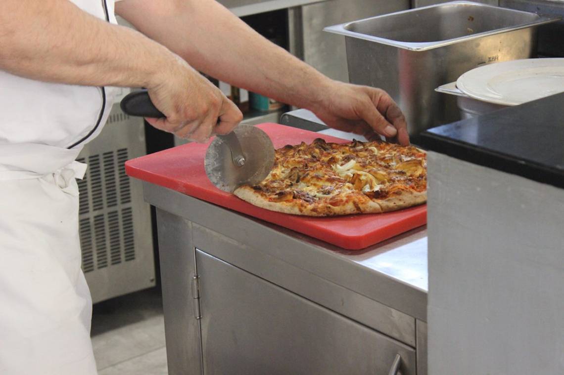Koch im Blue Aegean Hotel & Suites schneidet eine Pizza auf einem roten Schneidebrett in der Küche.