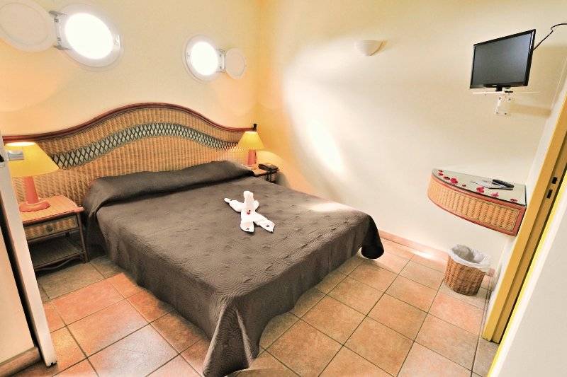 Ein Zimmer mit einem Bett, einem Fernseher und einem Nachttisch im Karibea Sainte Luce Hotel.