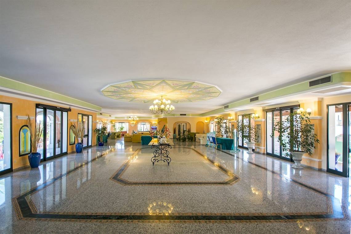 Empfangsbereich des Club Hotel Marina Beach mit hellem Innendesign, großen Fenstern und Dekorationspflanzen.