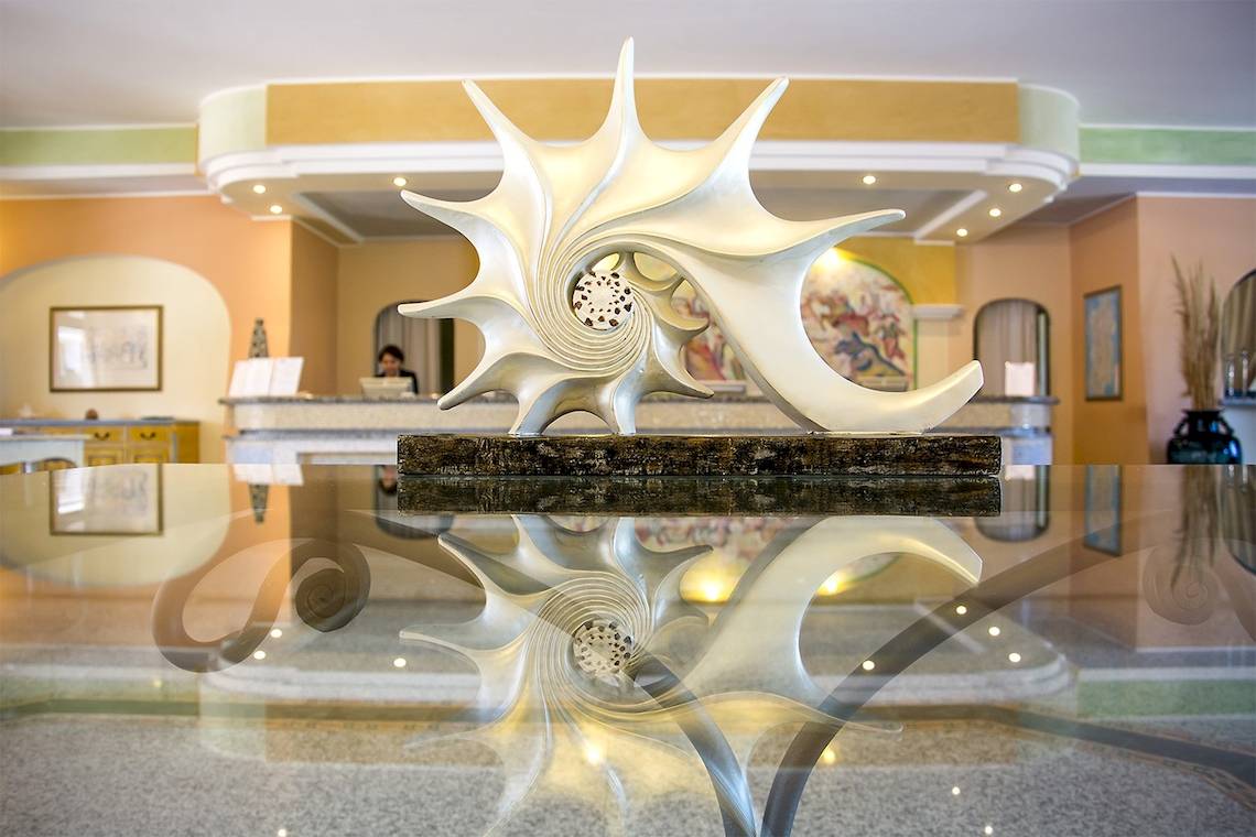Empfangsbereich des Club Hotel Marina Beach mit einer großen Muschelskulptur auf einem Glastisch.