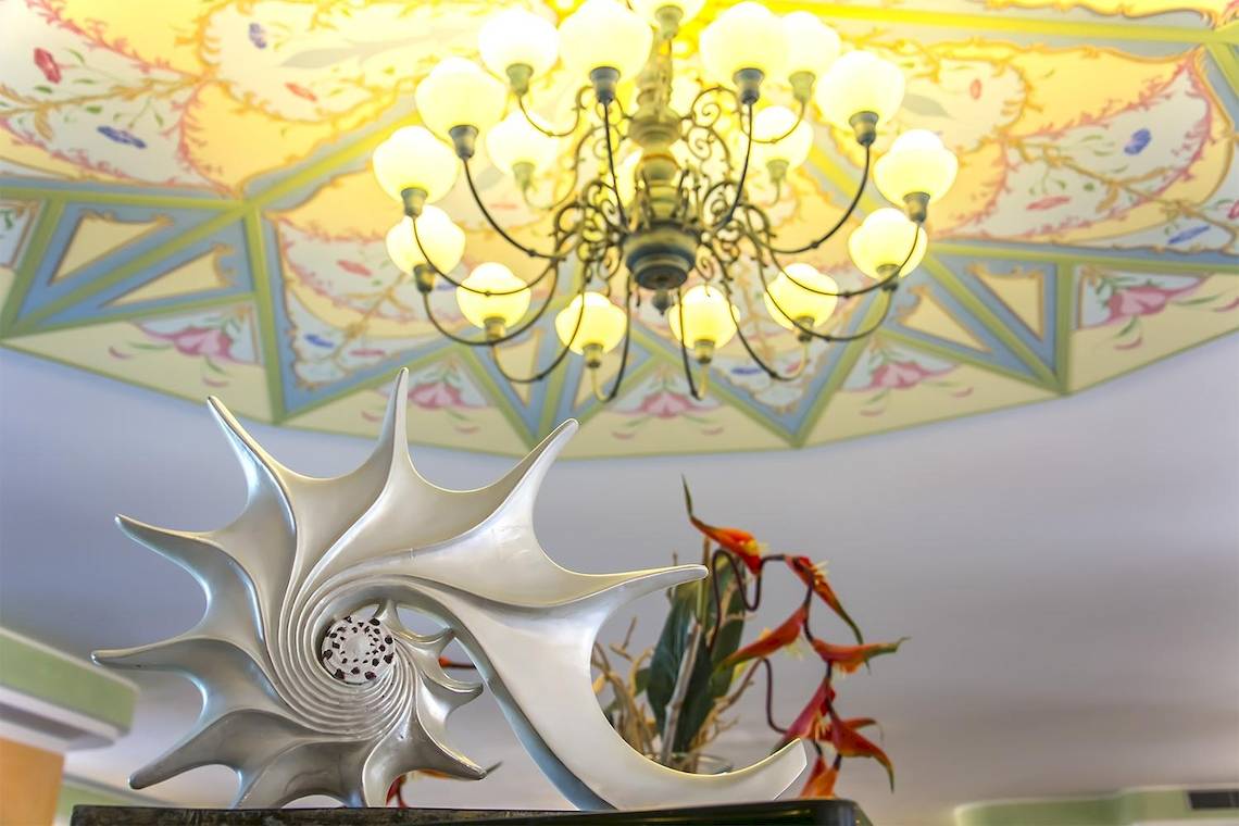 Ein Hotel-Lobby mit einer großen, silbernen Muschelskulptur und einer kunstvollen Deckenlampe.