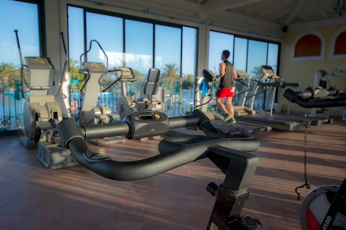 Fitnessstudio im Club Hotel Marina Beach mit Geräten und einem Mann, der auf einem Laufband läuft.