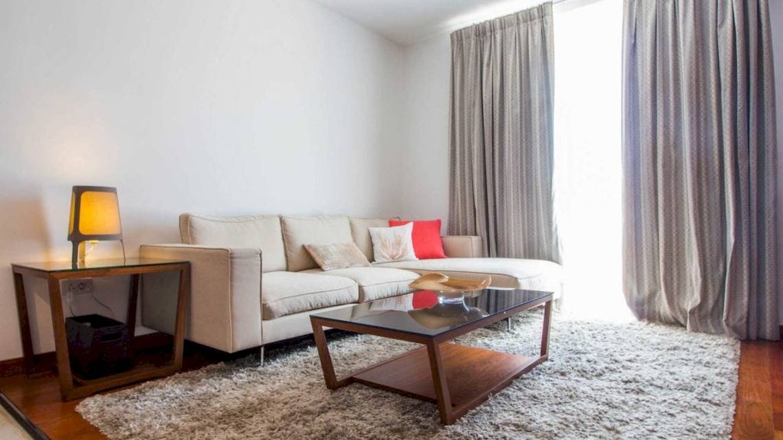 Ein Wohnzimmer mit einem weißen Sofa, einem Tisch, einer Lampe und einem Teppich.