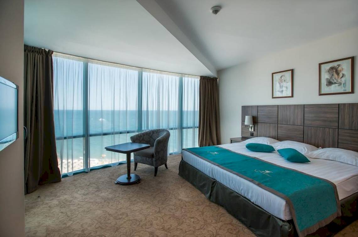 Zimmer im Marina Grand Beach Hotel mit Blick auf das Meer von einem großen Bett aus.