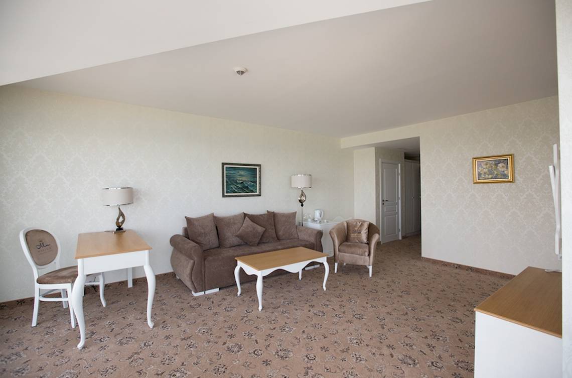 Wohnzimmer im Marina Grand Beach Hotel mit Sofa, Tisch, Stühlen und Bildern an der Wand.