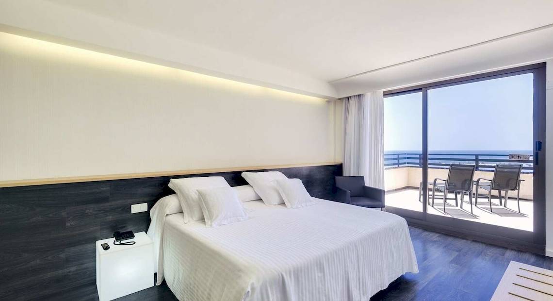 Hotelzimmer mit Balkon und Meerblick, Bett und Kissen, Stühle und Tisch draußen