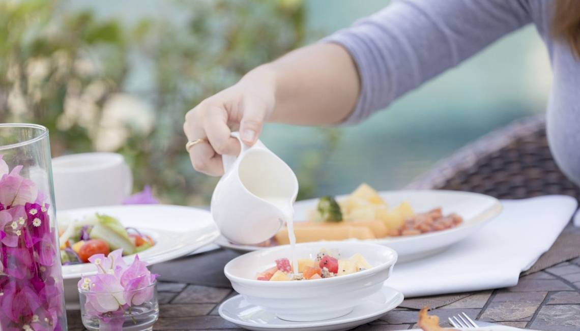 Frühstückstisch im Beyond Resort Krabi mit Schüssel, Tellern, Milch und Blumen.