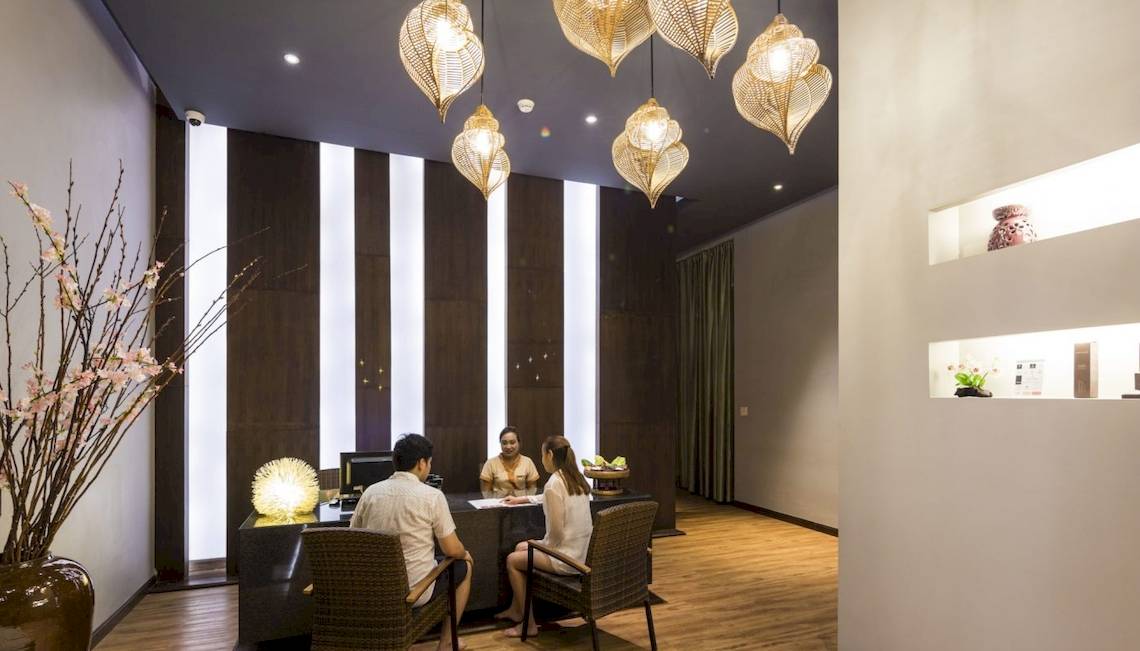 Innenansicht der Rezeption im Beyond Resort Krabi mit drei Personen, die an einem Tisch sitzen, und dekorativen Elementen wie Lampen und Pflanzen.