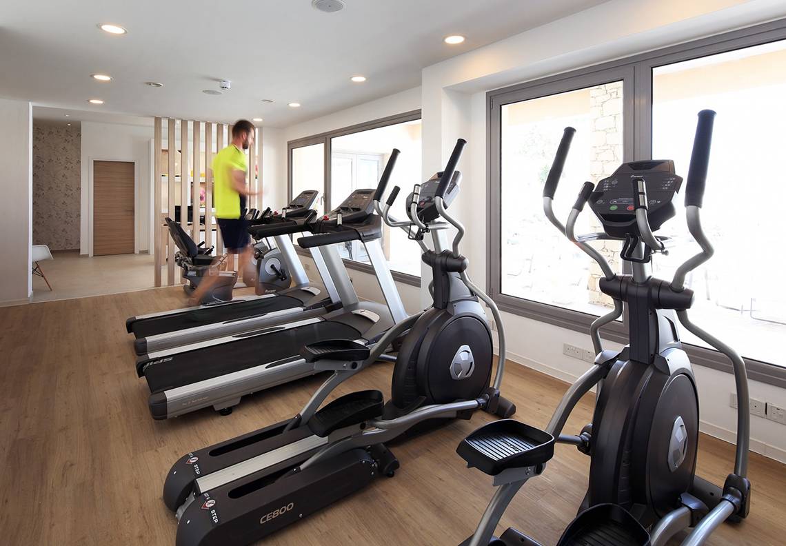 Fitnessraum im Louis St. Elias Resort & Waterpark mit mehreren Cardiogeräten und einem Mann, der läuft.