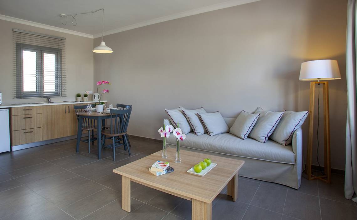 Wohnzimmer des Louis St. Elias Resorts mit Sofa, Tisch, Lampe und Küche im Hintergrund.