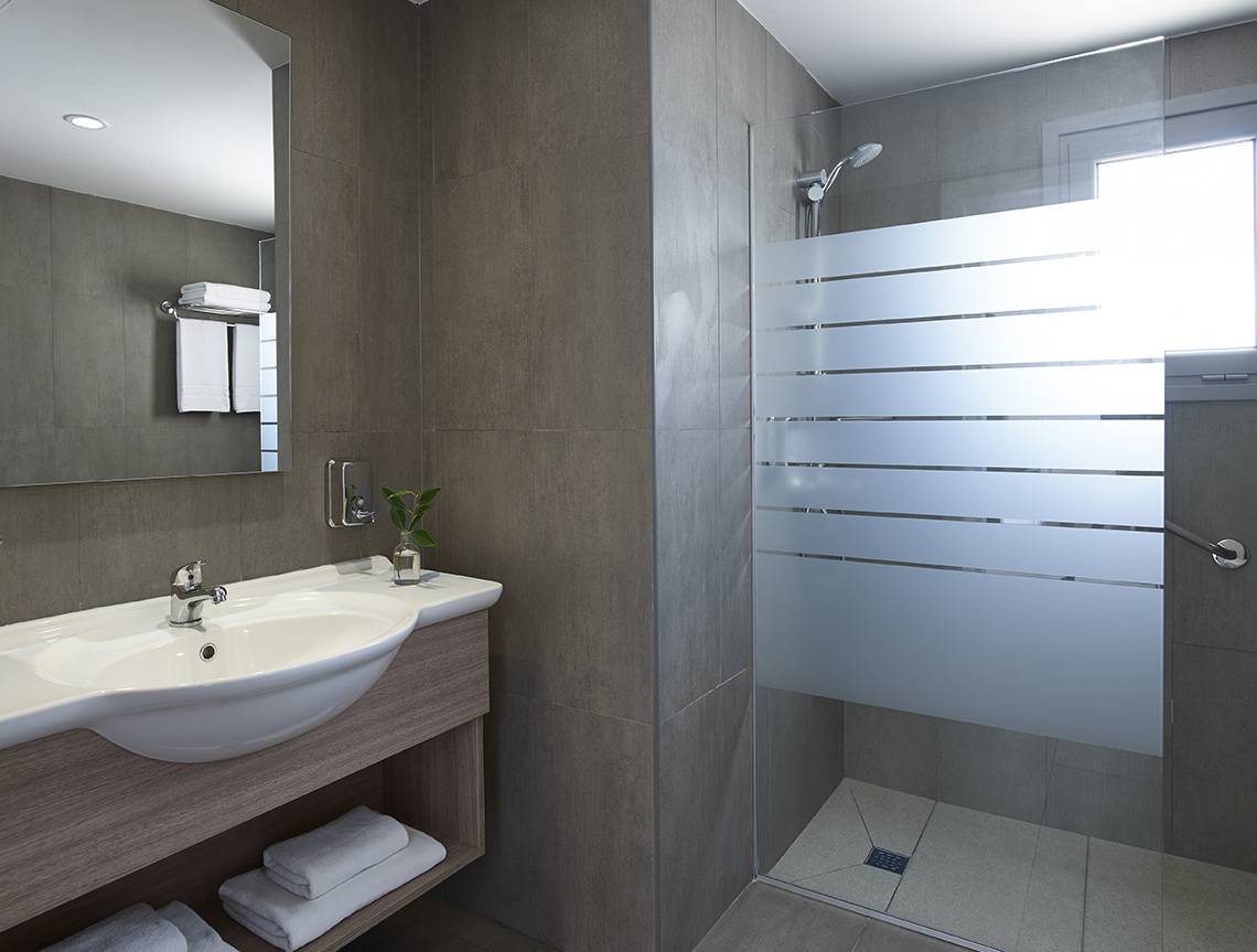 Badezimmer im Louis St. Elias Resort & Waterpark mit Waschbecken, Spiegel und Dusche.