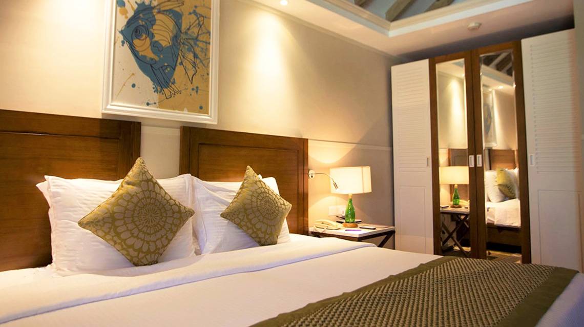 Hotelzimmer im Ellaidhoo Maldives by Cinnamon mit Bett, Kissen, Lampen und Gemälde an der Wand.
