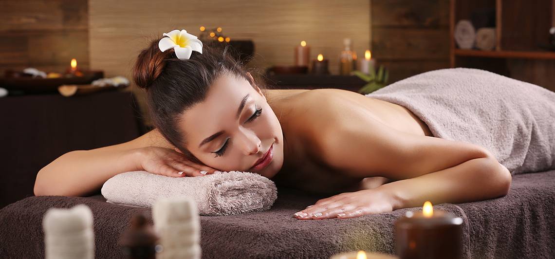 Eine Frau genießt eine Massagebehandlung im Ellaidhoo Maldives Spa mit Kerzen und Blütenblättern.