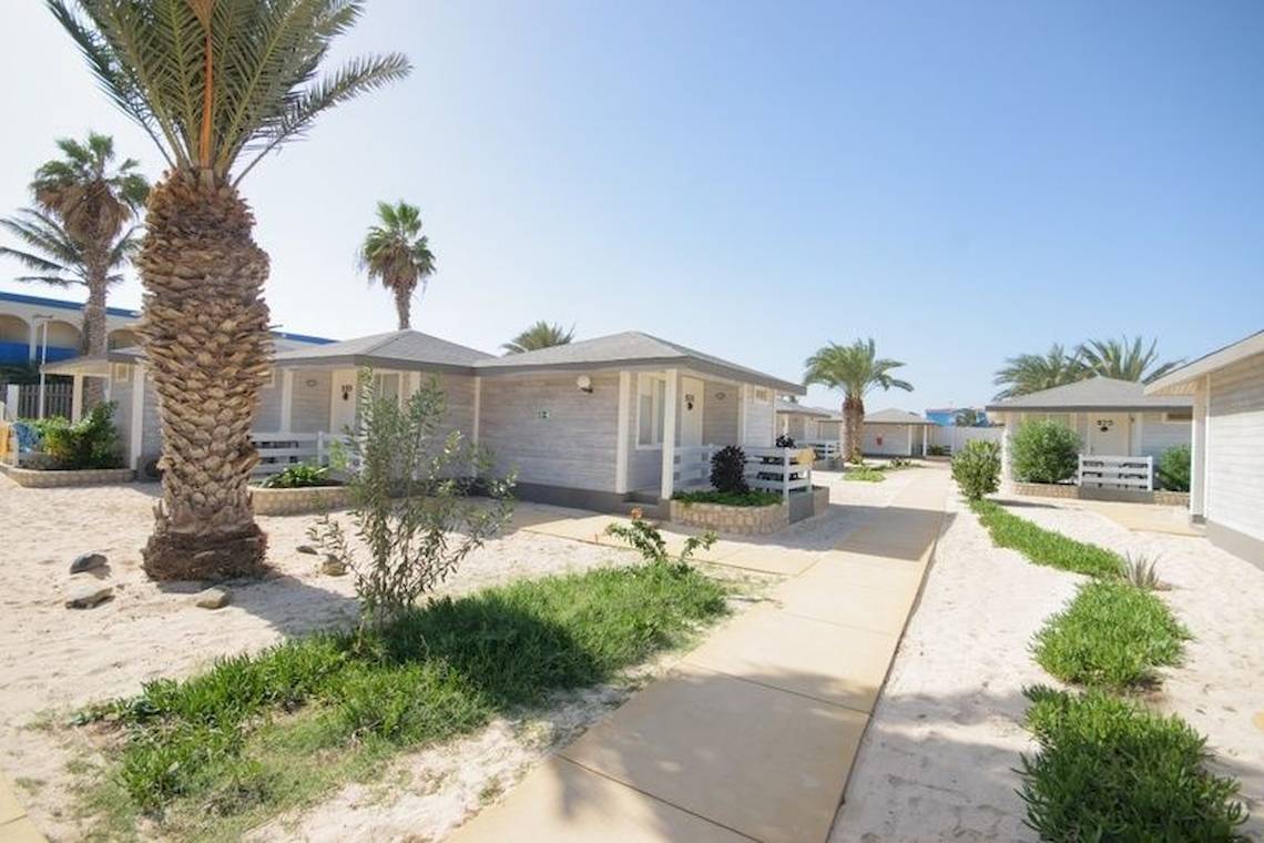 Reihe von weißen Bungalows am Strand, umgeben von Palmen und Pflanzen, Oasis Belorizonte Hotel.