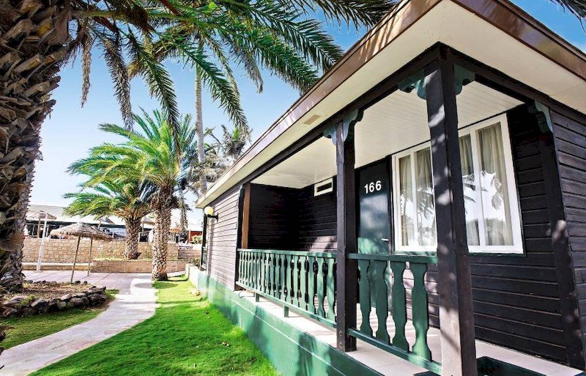 Außenansicht des Oasis Belorizonte Ferienhauses mit grüner Veranda und Palmen im Hintergrund.