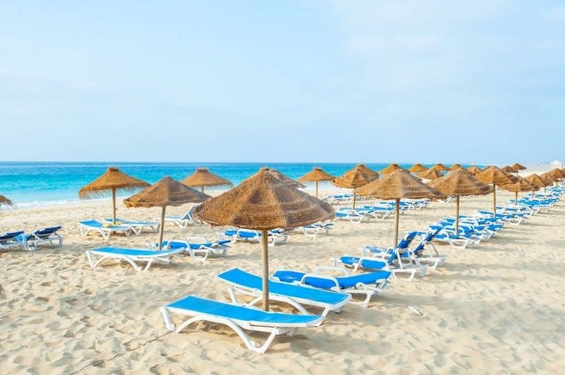 Strandszene im Oasis Belorizonte Hotel mit vielen Sonnenliegen und Sonnenschirmen.