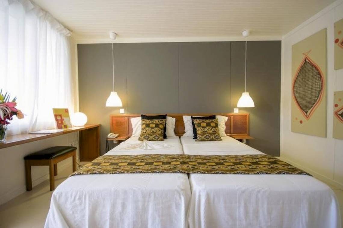 Doppelbett-Zimmer im Oasis Belorizonte Hotel mit zwei weißen Betten, grauen Wänden und einer Fensterbank mit Blumen.
